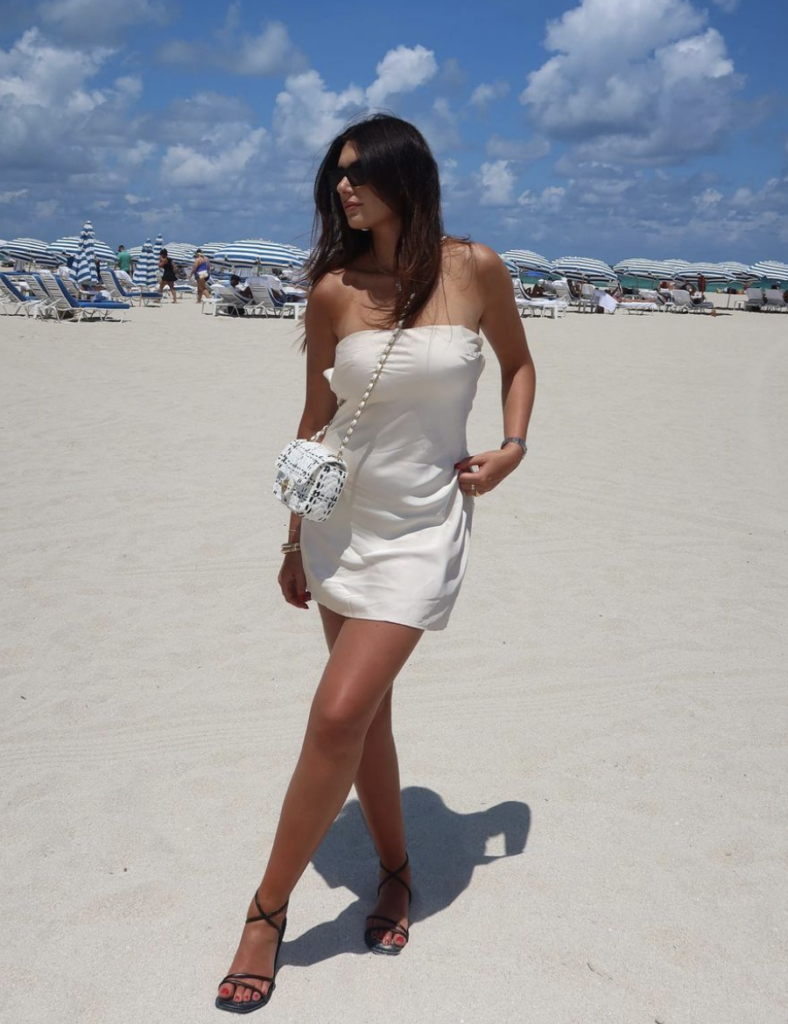 A minimalist slip dress in cream, accessorized with a patterned bag and strappy sandals, provides a chic option for beachside activities.